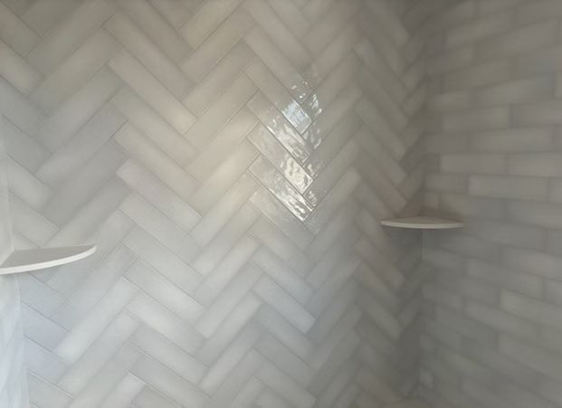 Herringbone tile shower with two corner shelves and soft light reflecting on the walls
