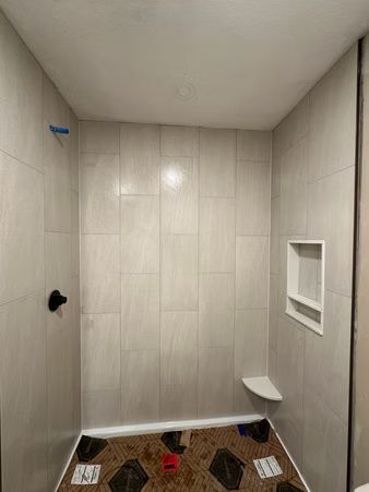 Small tiled shower stall with a bench, shelf niche, and cleaning supplies on the floor.