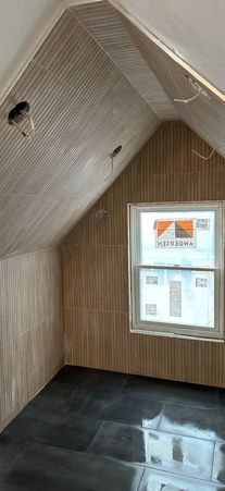 Empty attic room with sloped wood-paneled walls, a small window, and a glossy black floor.