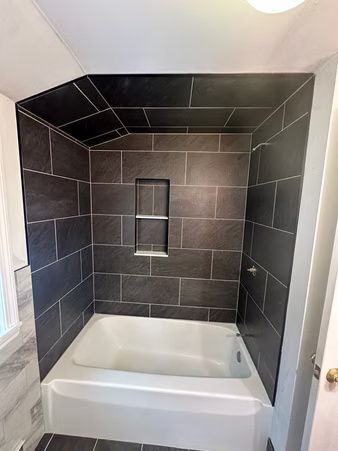 Small bathroom shower-tub with dark tile walls and a recessed niche above a white bathtub.