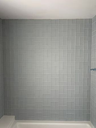 Empty tiled shower stall with light gray walls and white base.