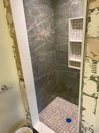 Partially tiled shower stall with dark gray walls, mosaic floor, and built-in shelves