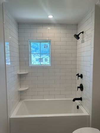 White tiled bathroom with a bathtub, window, and black shower fixtures