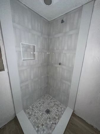 Tiled shower stall with gray walls, mosaic floor, and a small recessed niche.