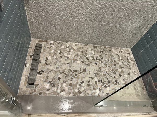 Small tiled shower floor with gray pebble mosaic, drain, and glass door panel