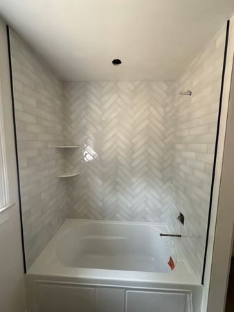 Empty white tiled bathtub alcove with herringbone backsplash and unfinished fixture openings