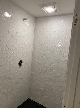 Small white-tiled shower stall with a ceiling light and dark shower floor