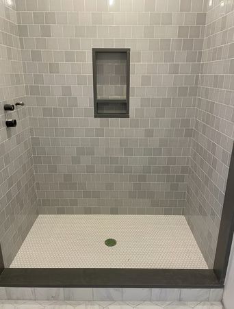 Empty gray-tiled shower stall with a recessed shelf and central drain