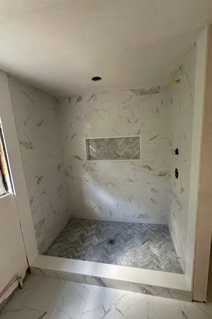 Empty tiled shower stall with marble-pattern walls and a small recessed shelf.