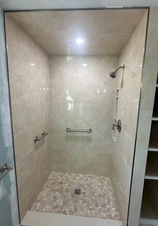 Empty tiled shower stall with beige walls, mosaic floor, grab bars, and shower fixtures