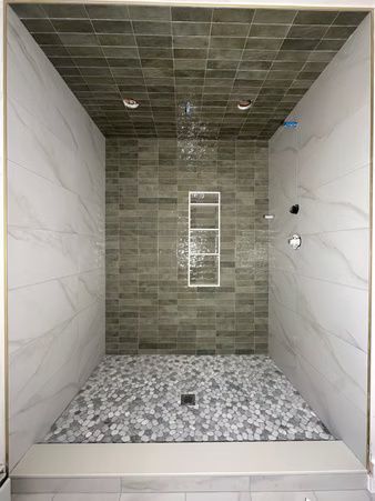 Empty tiled walk-in shower with gray mosaic floor and white marble-look side walls.