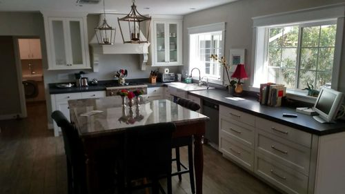 Bright modern kitchen with white cabinets, dark countertops, island, and large windows opening to a view outside