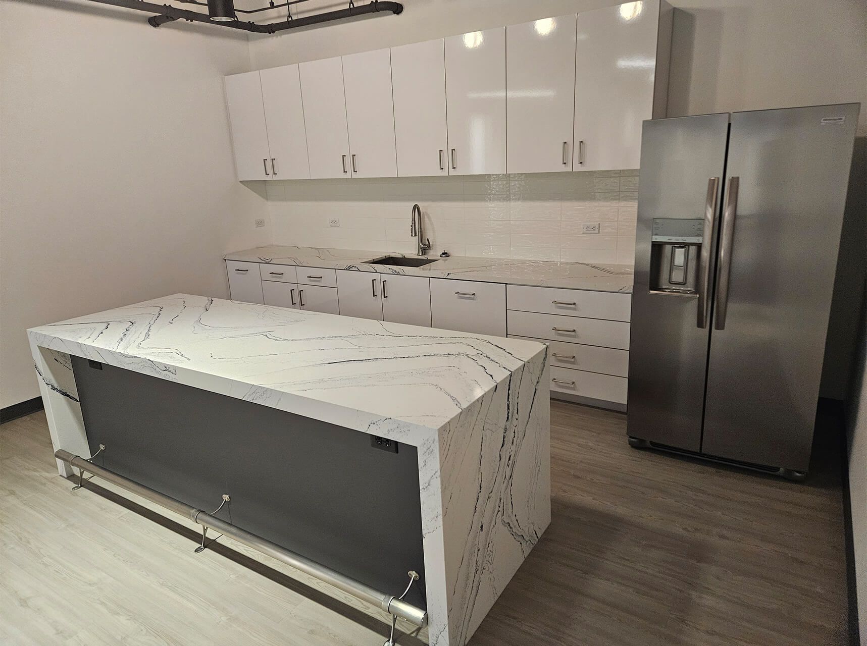 Modern kitchen with white cabinets, marble island, and stainless steel refrigerator