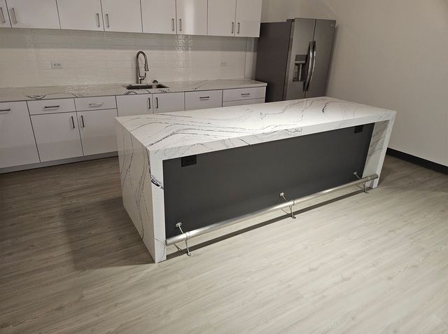 Modern kitchen with white cabinets and a large marble island centered in the room.