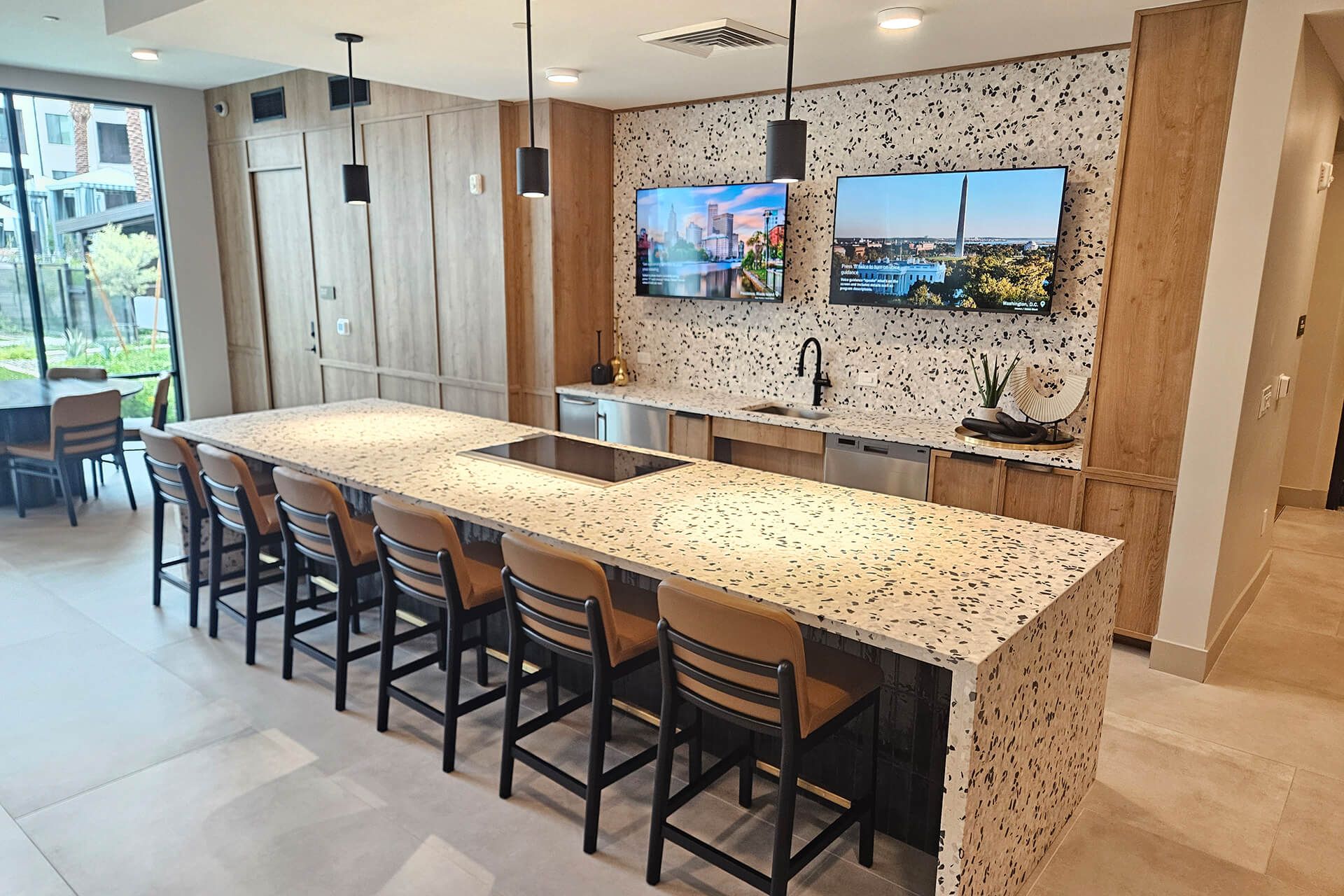 Modern kitchen with a large island, barstools, and wall-mounted TVs in a bright open-plan home