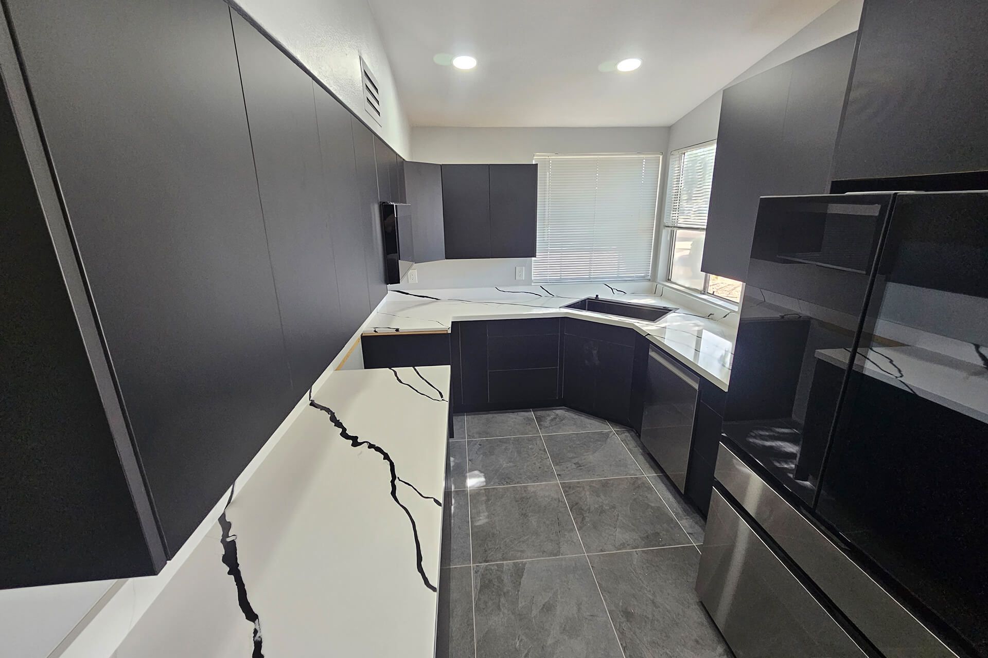 Modern kitchen with dark cabinets, white countertops, tiled floor, and stainless steel appliances.
