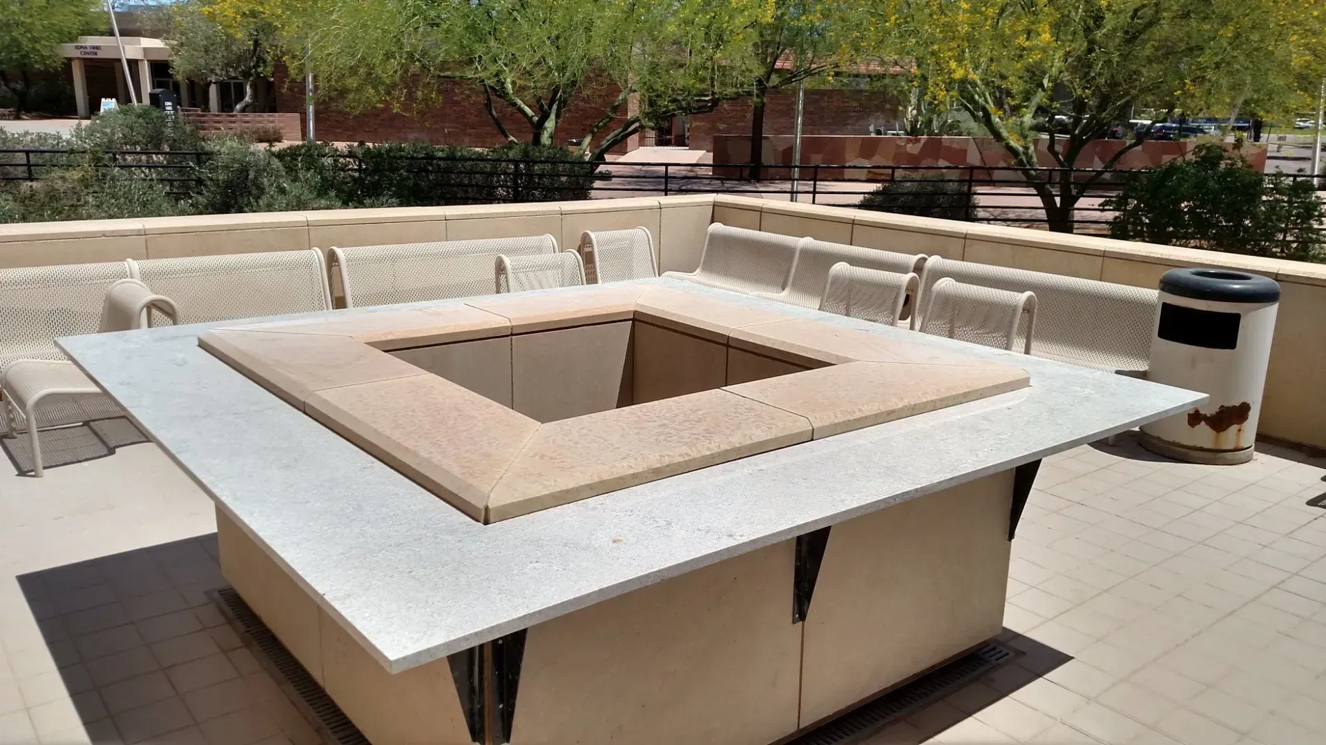 Outdoor square concrete fire pit with built-in benches in a sunny courtyard