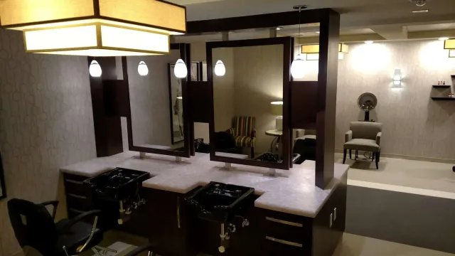 Empty vanity with large mirror, lit pendant lamps, and a chair in a bathroom or dressing room.