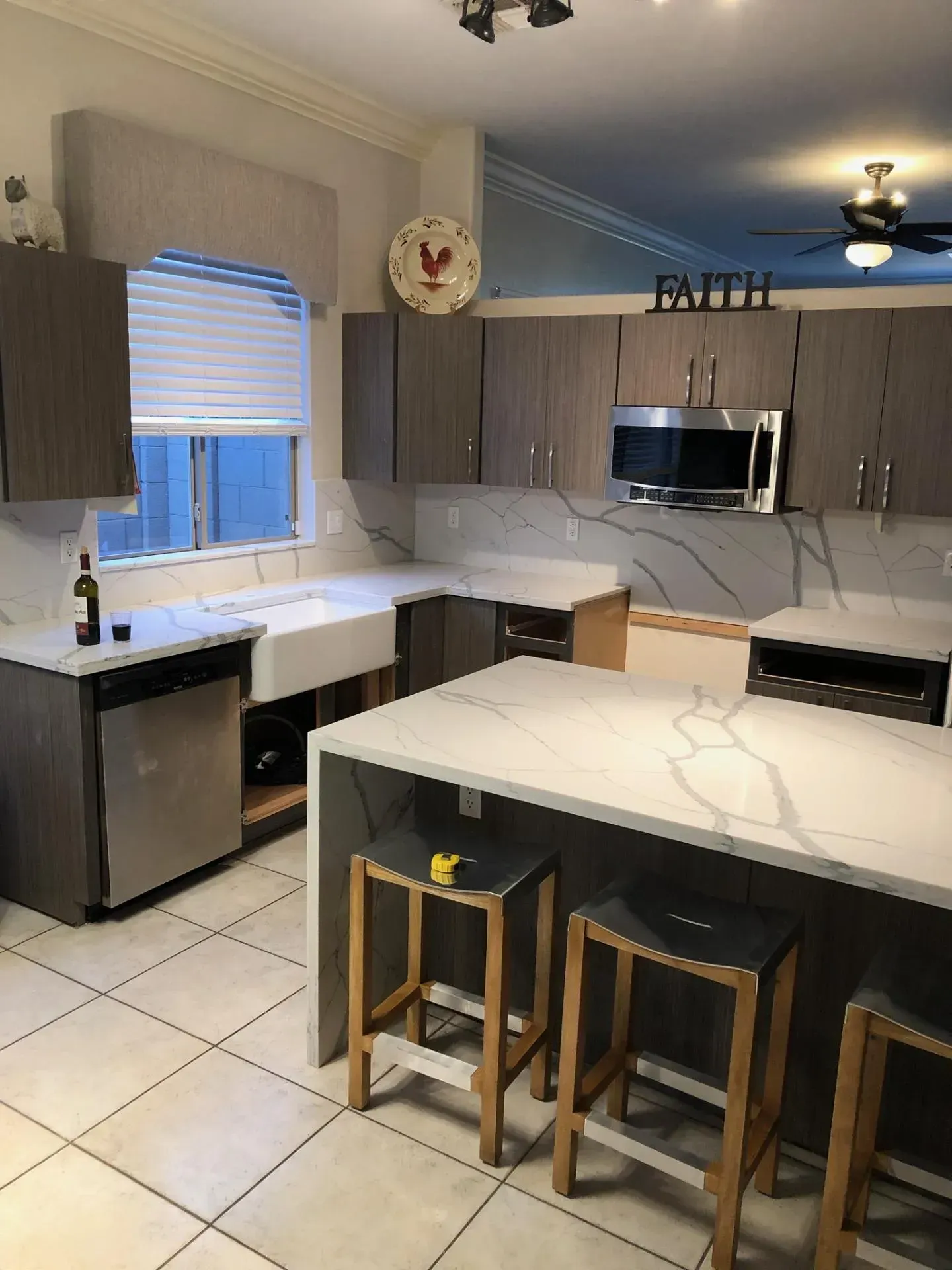 Modern kitchen with gray cabinets, white countertops, island stools, and stainless steel appliances.