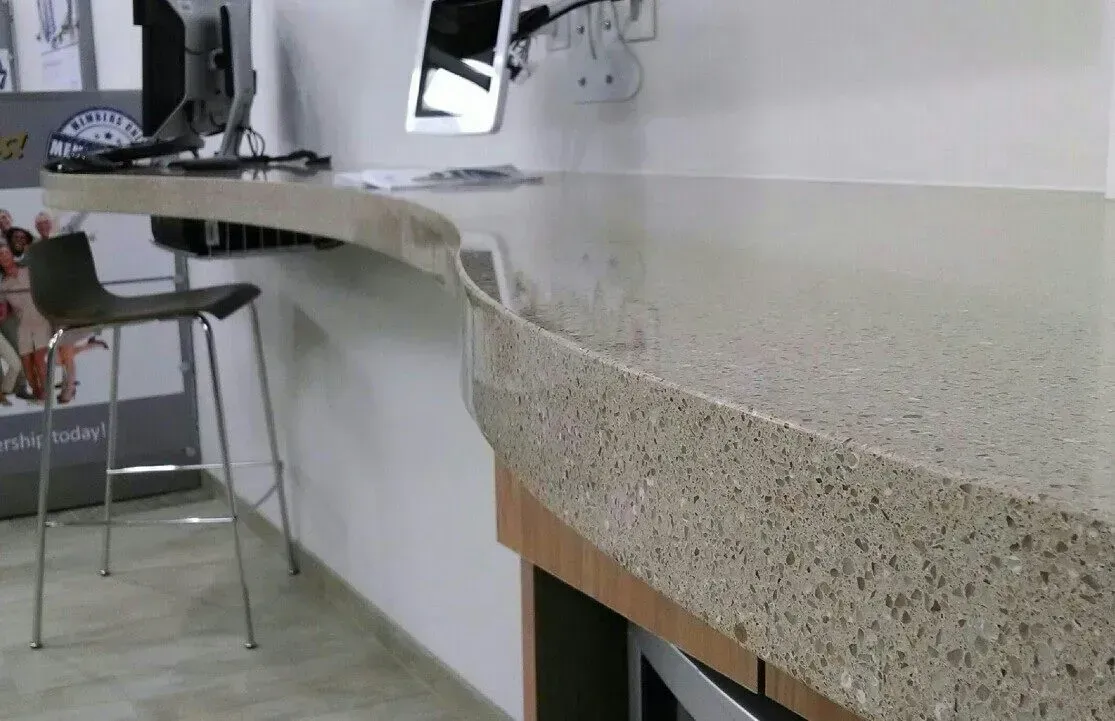Curved speckled countertop in a modern kitchen with stools and a sink area in the background