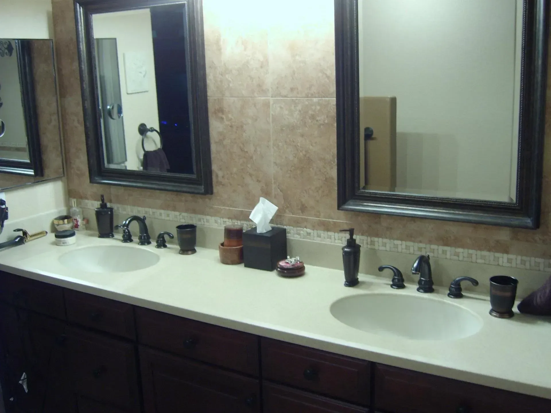 Bathroom vanity with double sinks, dark wood cabinets, and mirrors above a beige countertop