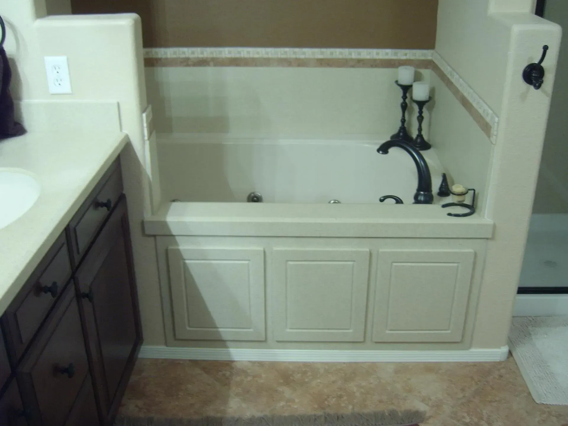 Bathroom with a built-in tub, dark vanity, white counters, and beige tile surround.