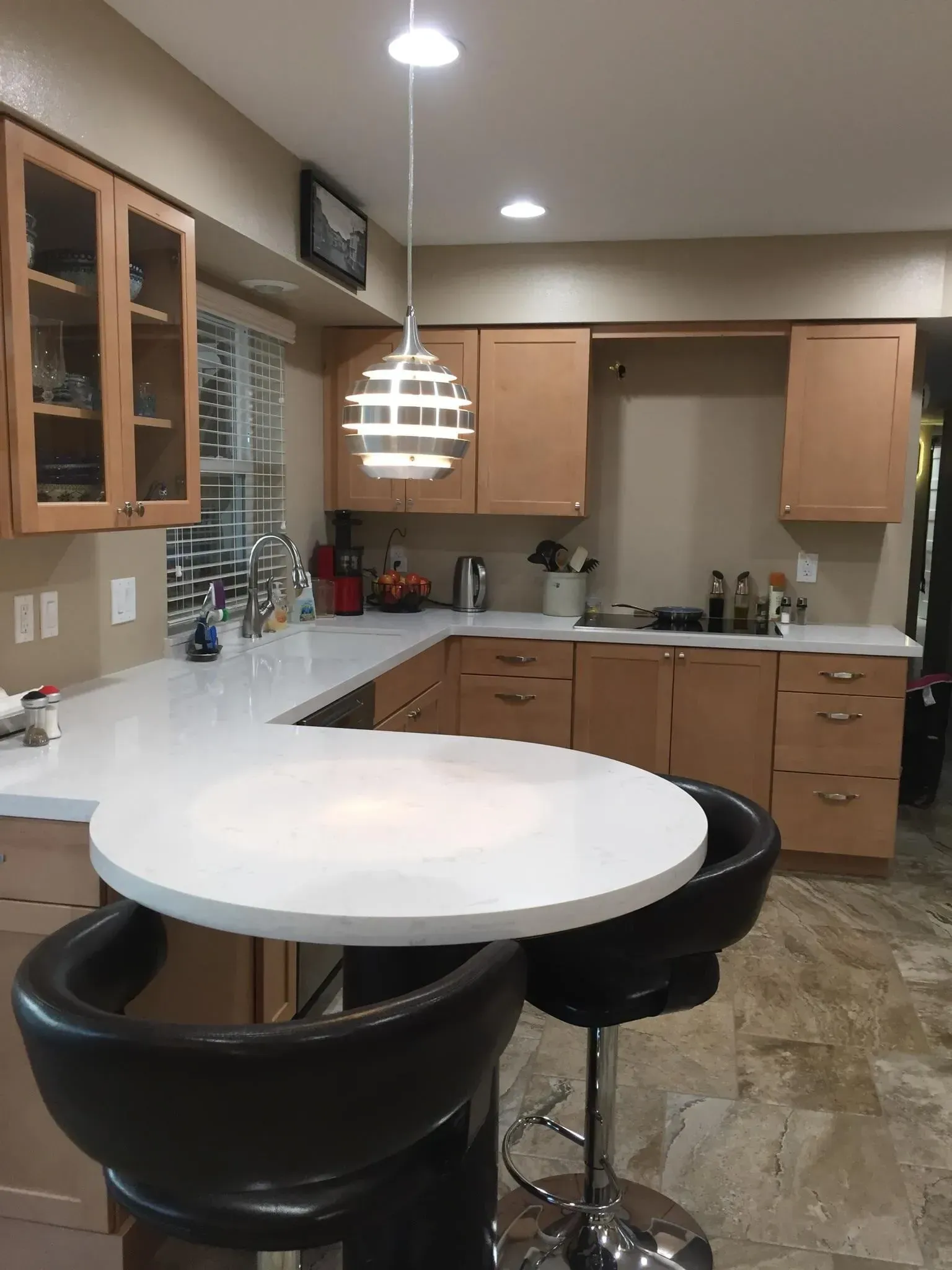 Small kitchen with wood cabinets, tiled backsplash, round white table, and black barstools under pendant lighting.