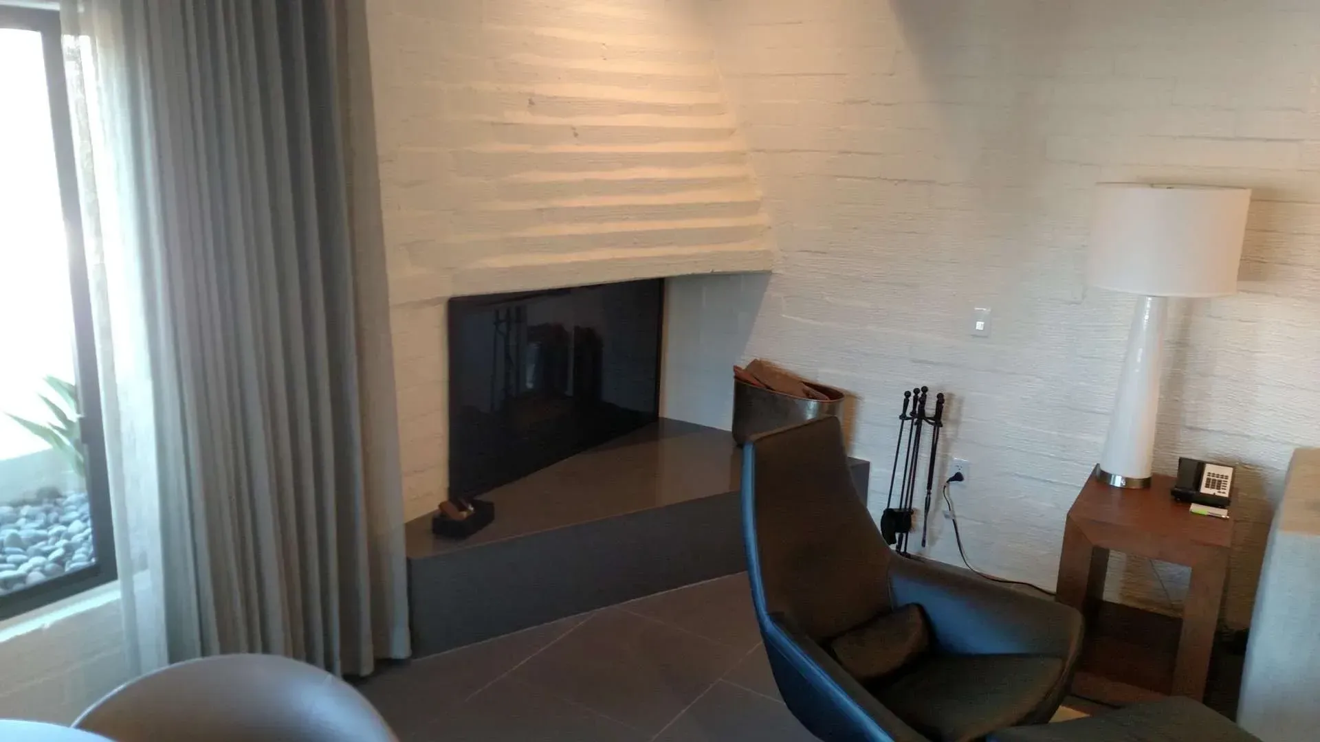 Modern living room with fireplace, curtains, lounge chair, floor lamp, and side table