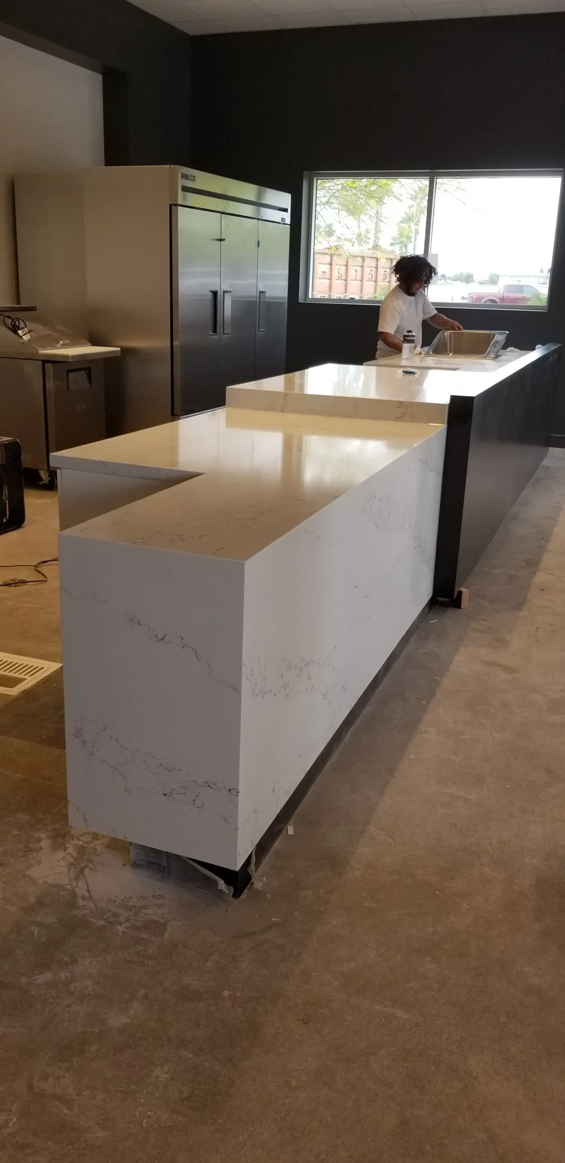 Modern kitchen with white island, stainless fridge, and person at a window counter