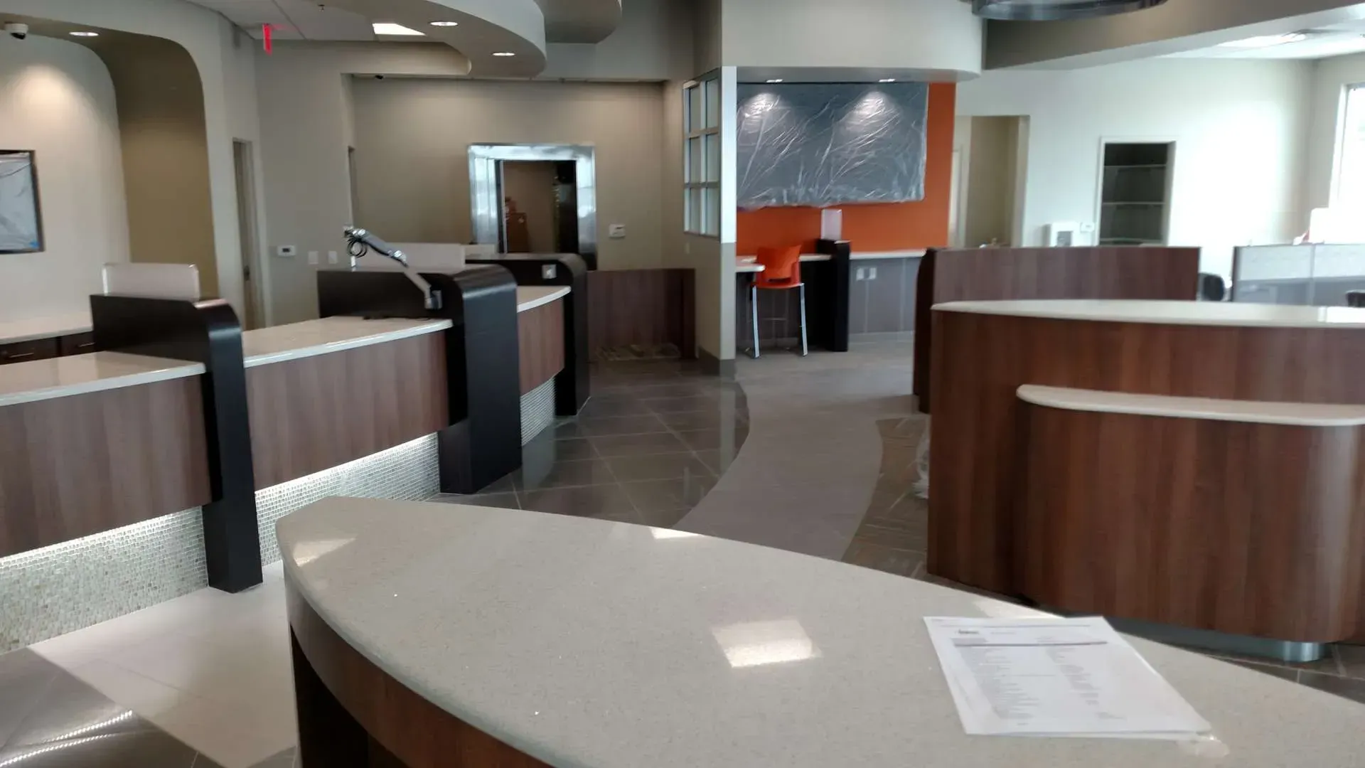 Empty modern bank lobby with curved wood counters, gray flooring, and bright overhead lighting