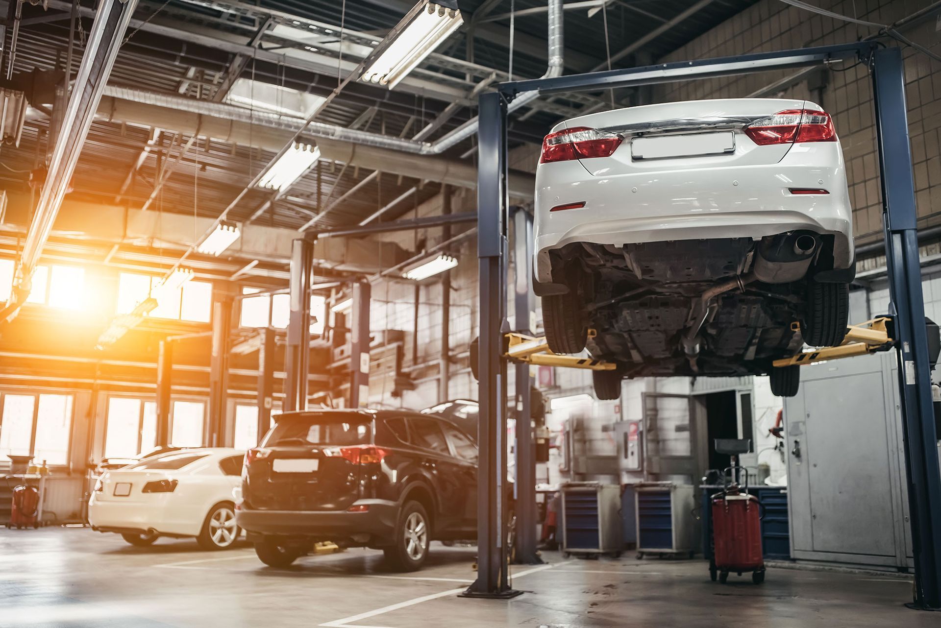Cars in a bright auto repair shop, with one white sedan raised on a lift.