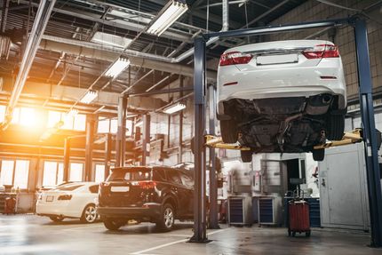Cars in a bright auto repair shop, with a white sedan raised on a lift.