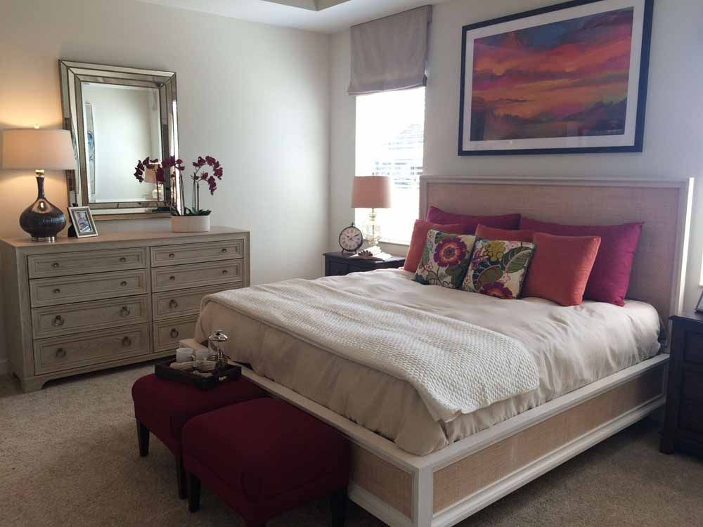 a bedroom with a large bed , dresser , mirror and ottoman