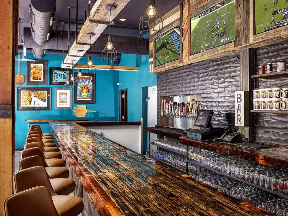 a long bar in a restaurant with a lot of stools and televisions on the wall