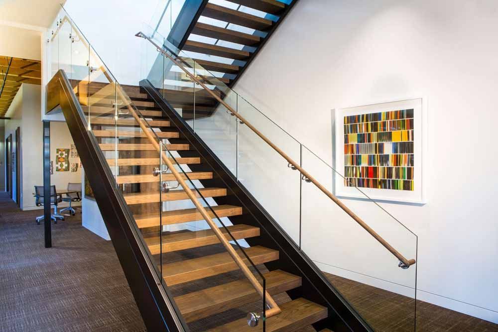 a wooden staircase with a glass railing and a picture on the wall
