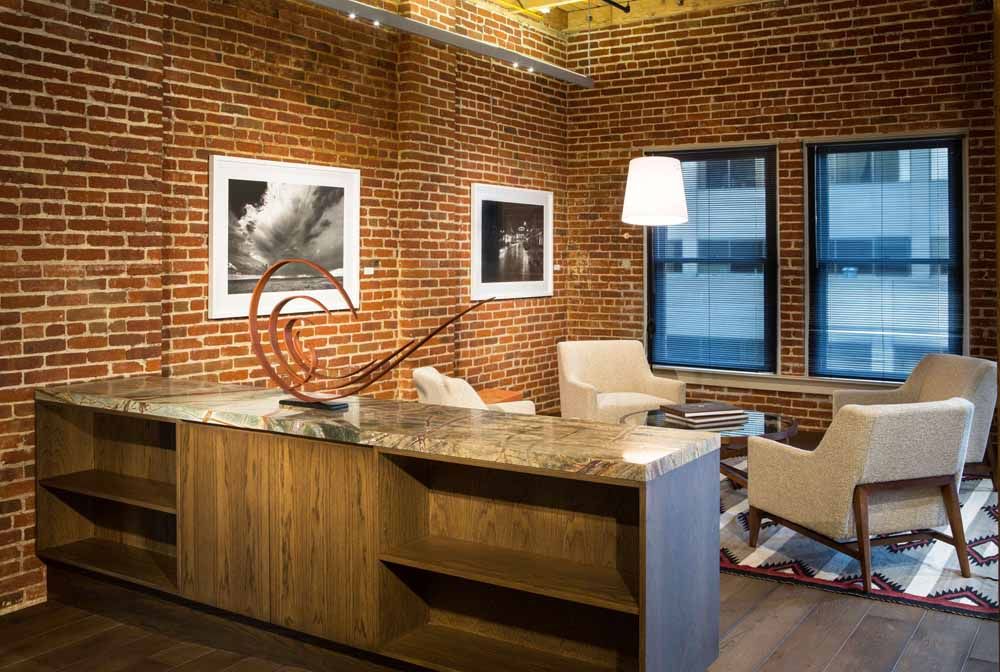 a living room with a brick wall , chairs , a table and a lamp .