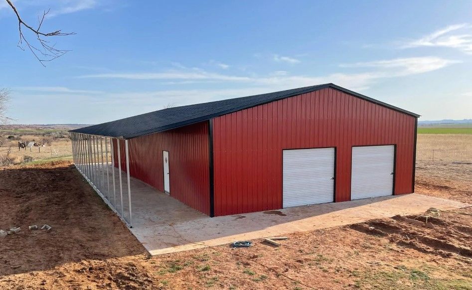 A red metal building with two garage doors is sitting in the middle of a dirt field