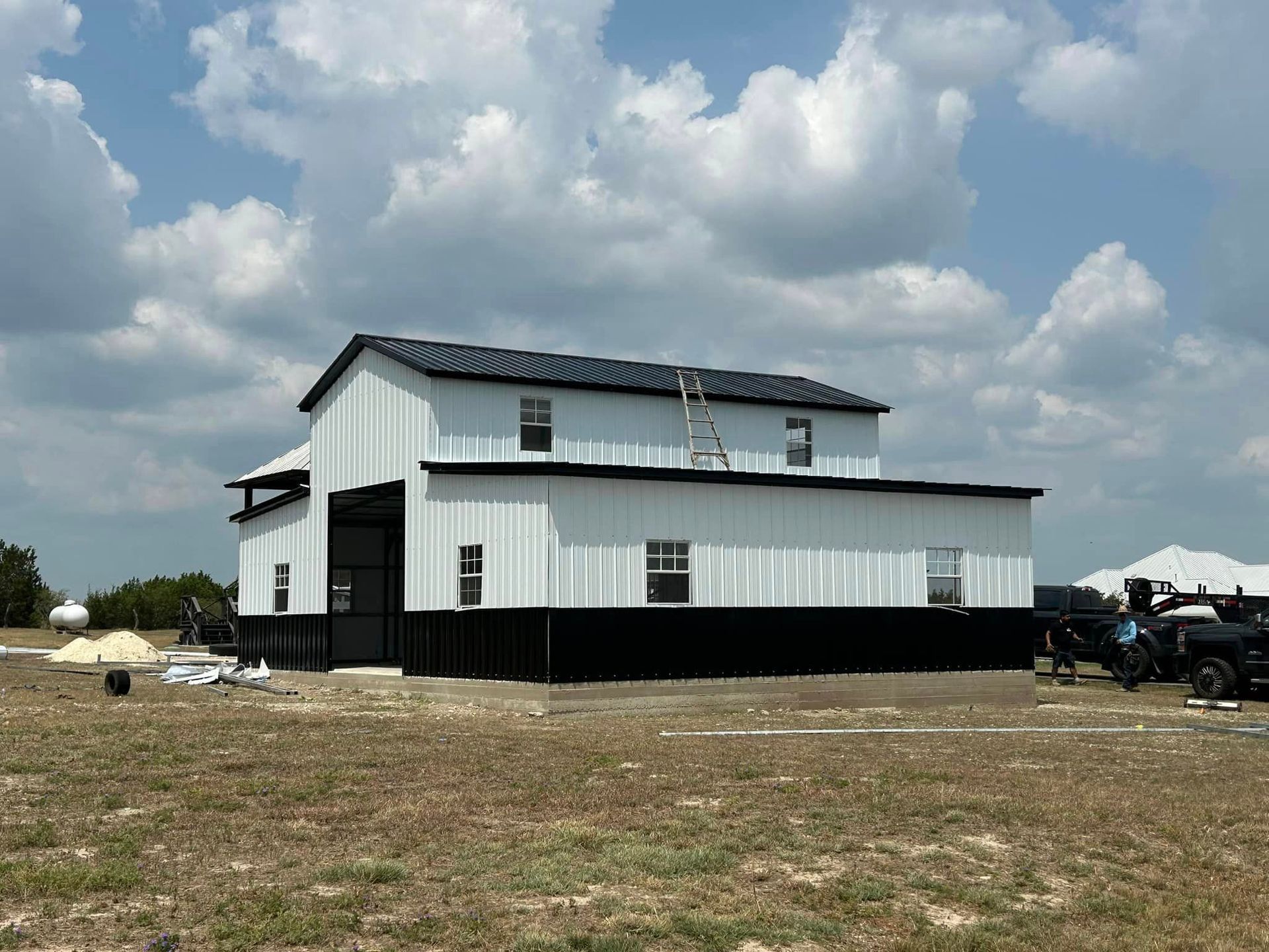 A large white barn with a black roof is sitting in the middle of a field