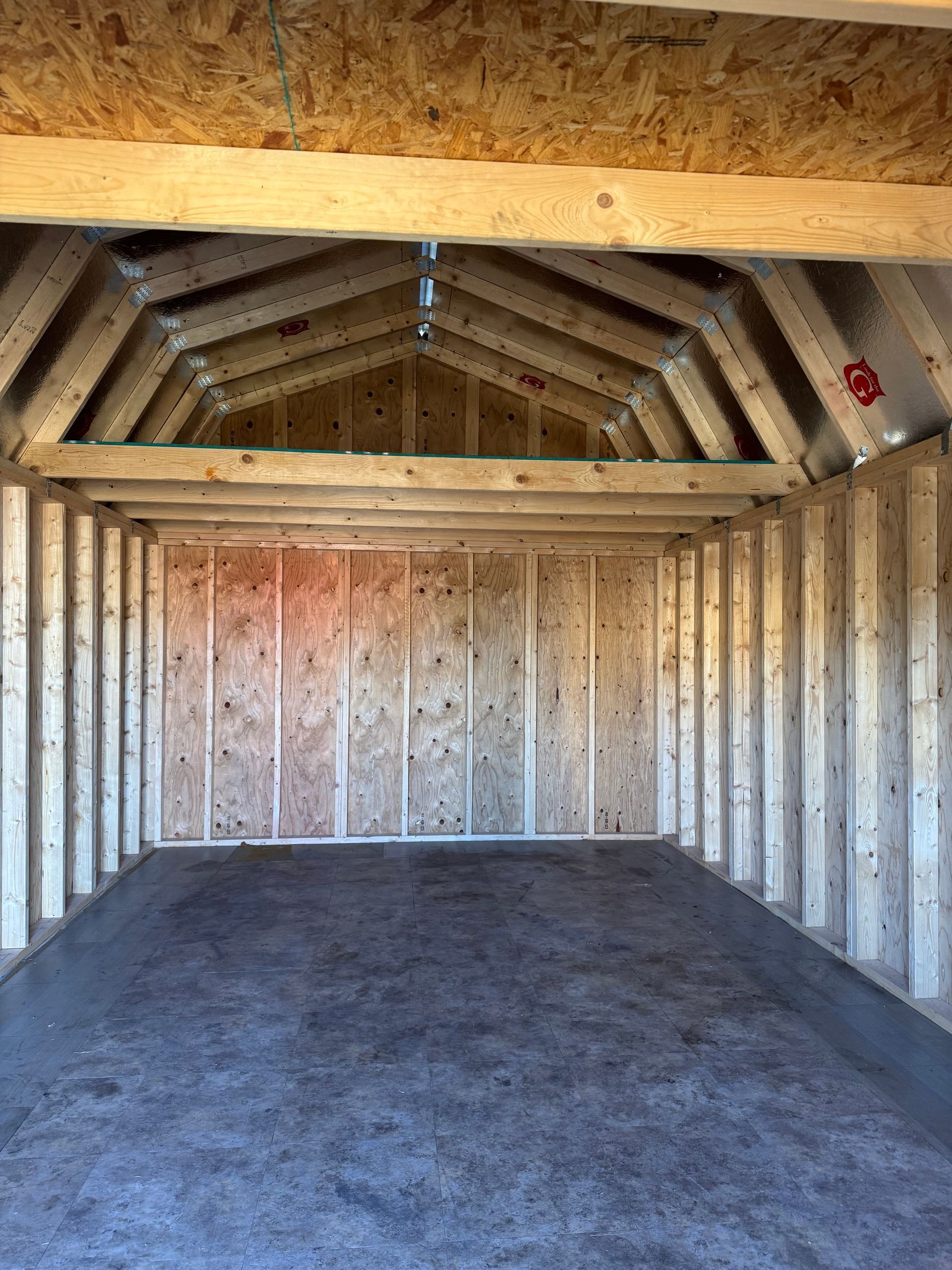 Interior of a wooden shed with plywood walls, a dark floor, and an angled ceiling.