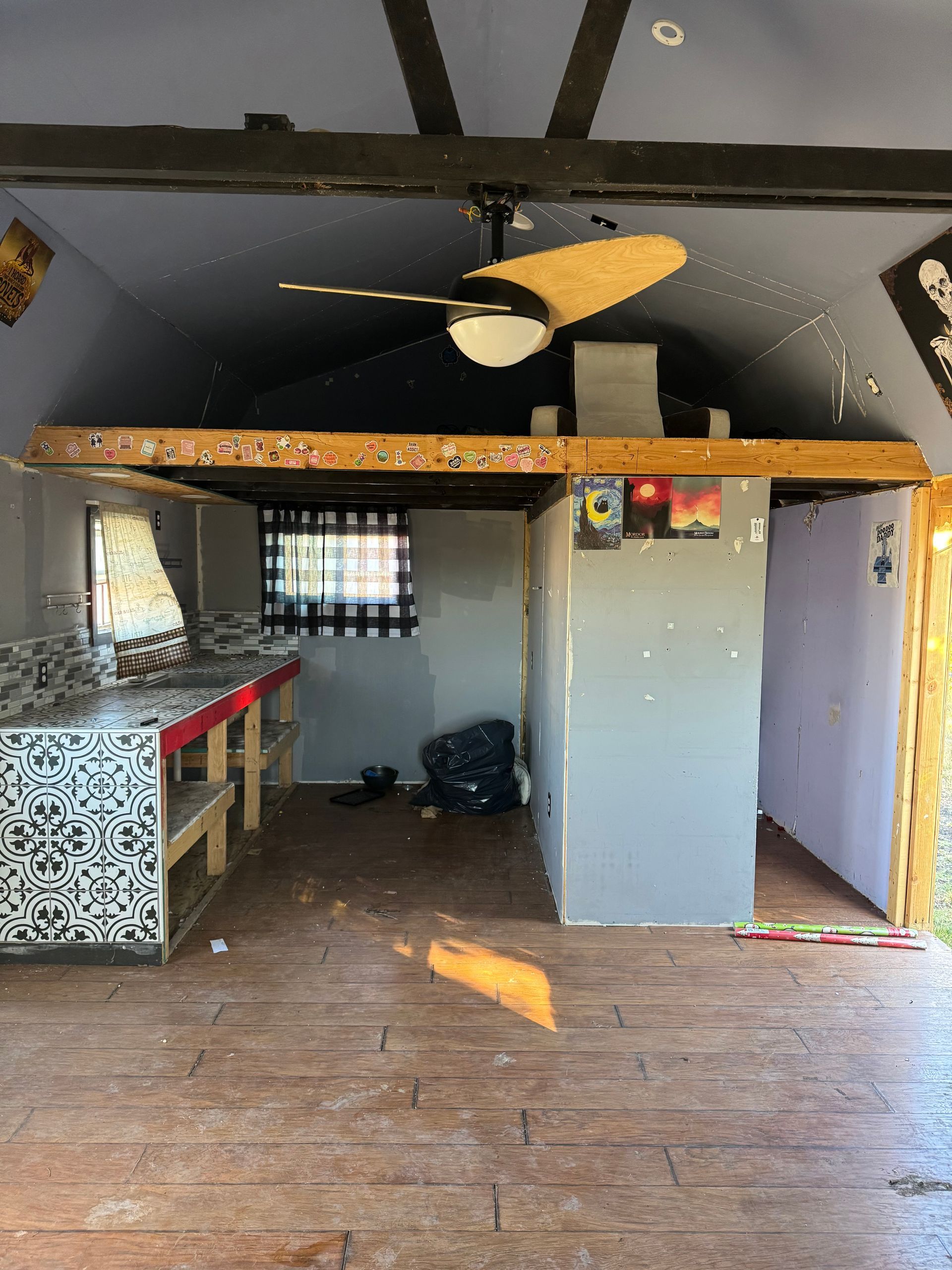 Interior of a small, unfinished cabin with exposed beams, ceiling fan, and partially built walls.