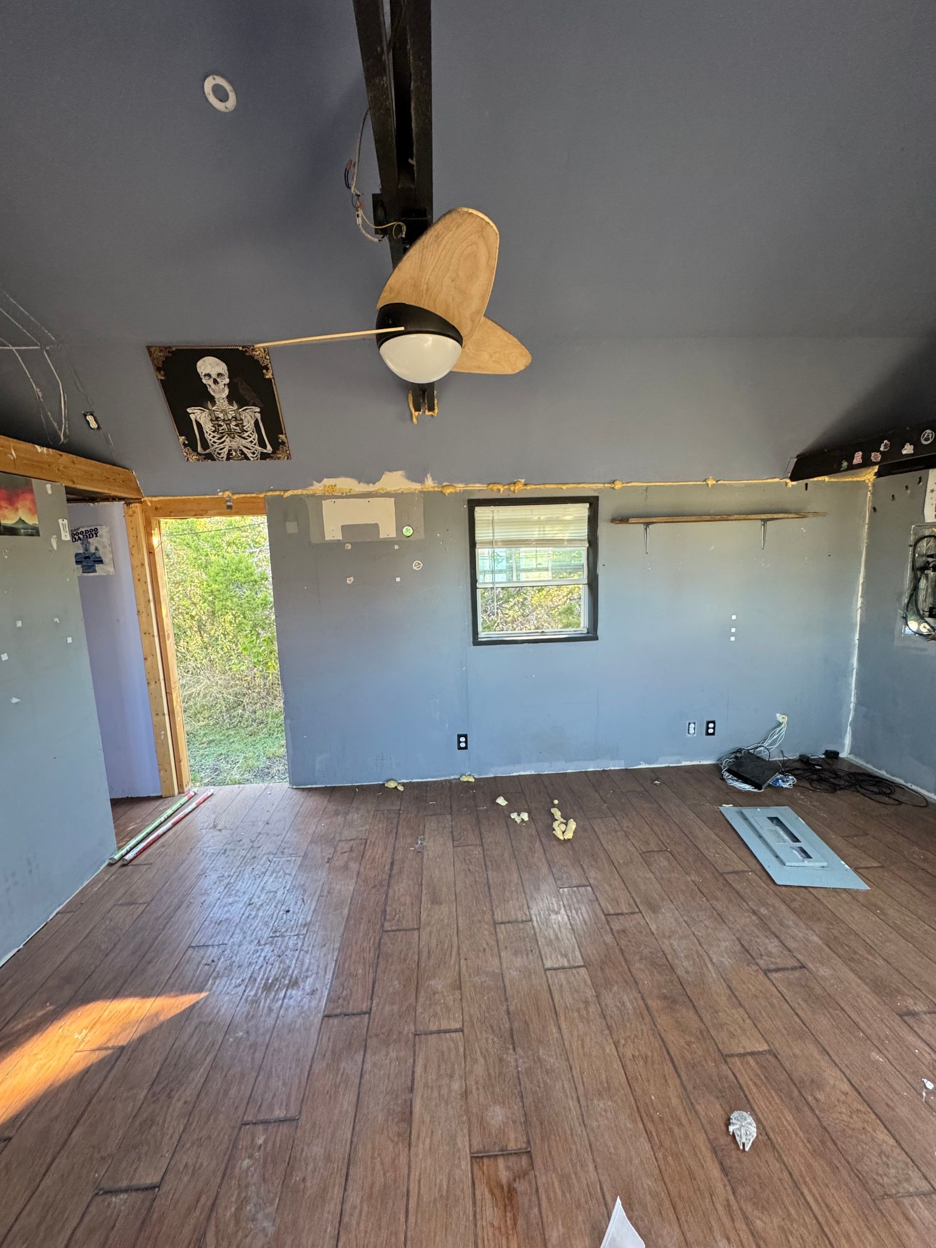 Empty room with wood floor, blue walls, a ceiling fan, and an open doorway leading outside.
