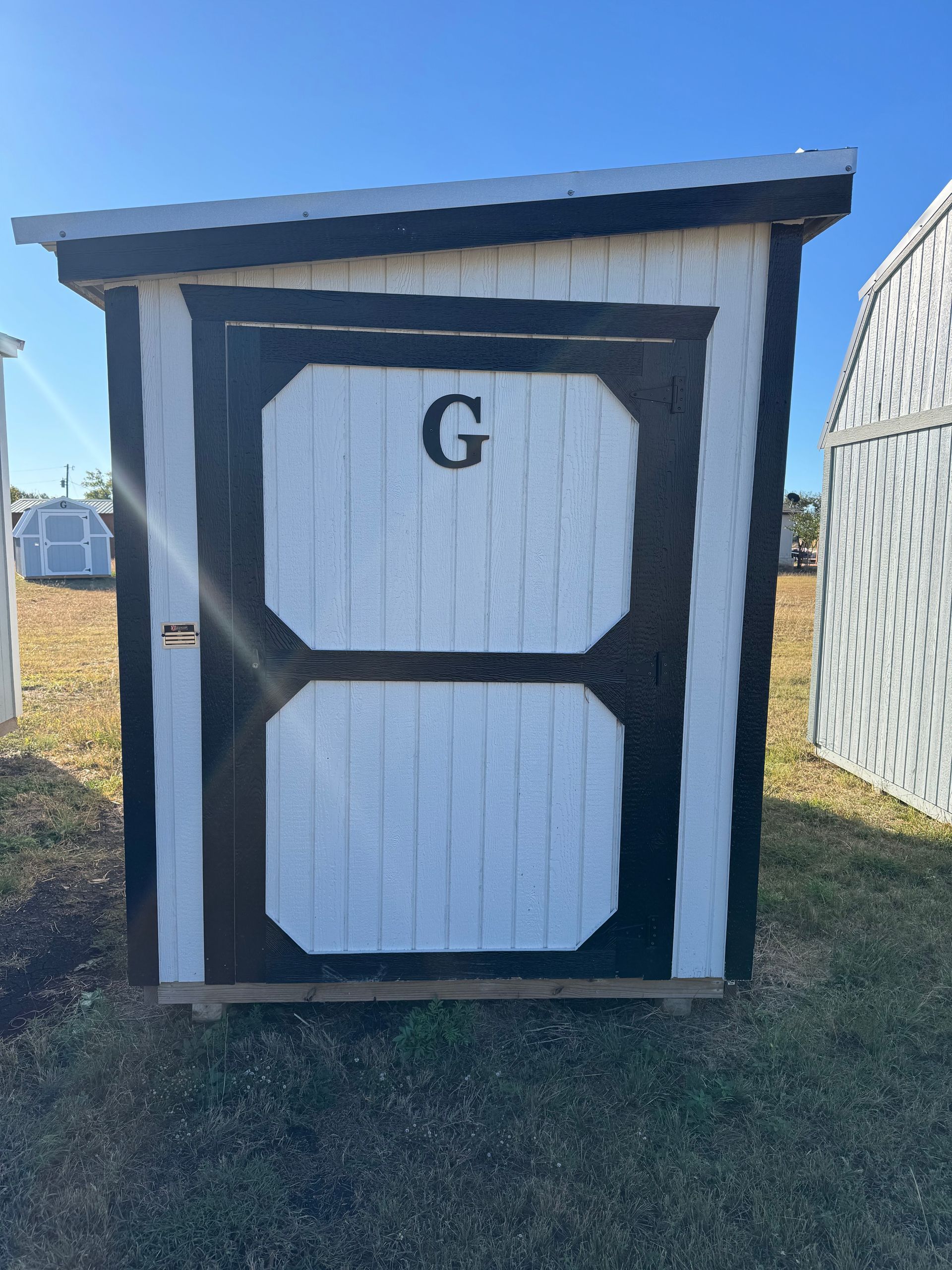 Black and white storage shed on grass, marked with a 
