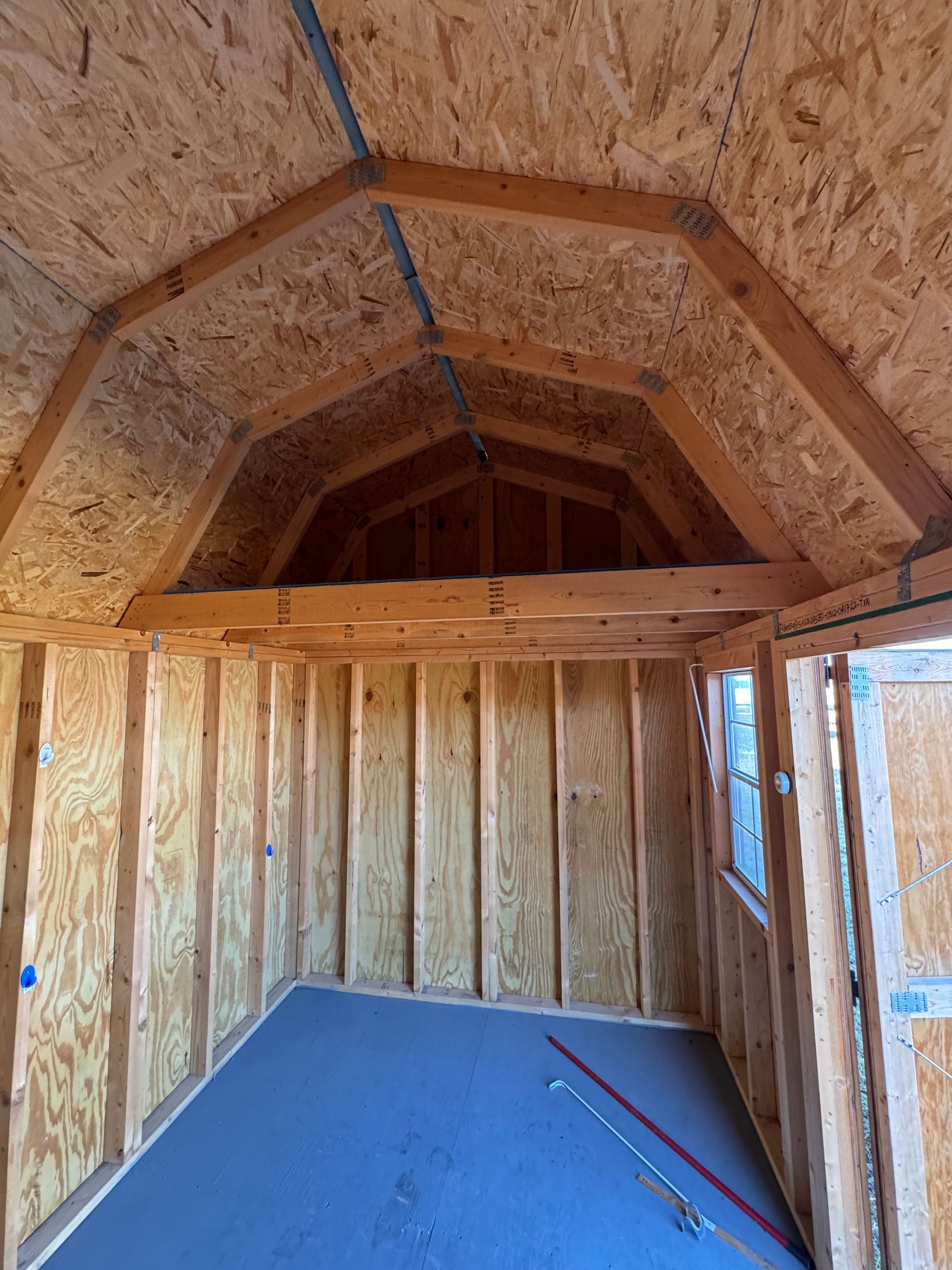 Interior view of unfinished shed with wooden frame walls, arched ceiling, and gray floor.