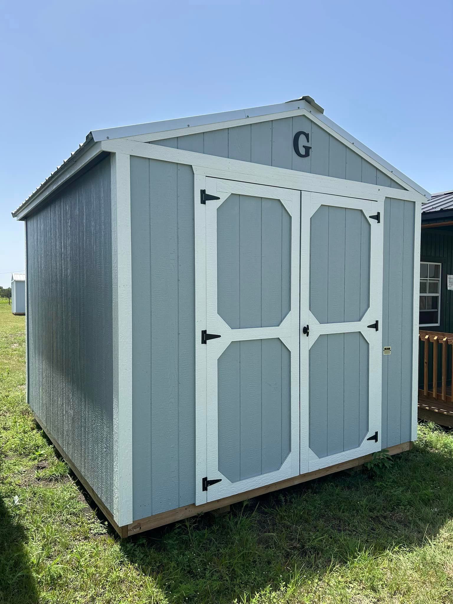 A gray and white shed is sitting in the middle of a grassy field