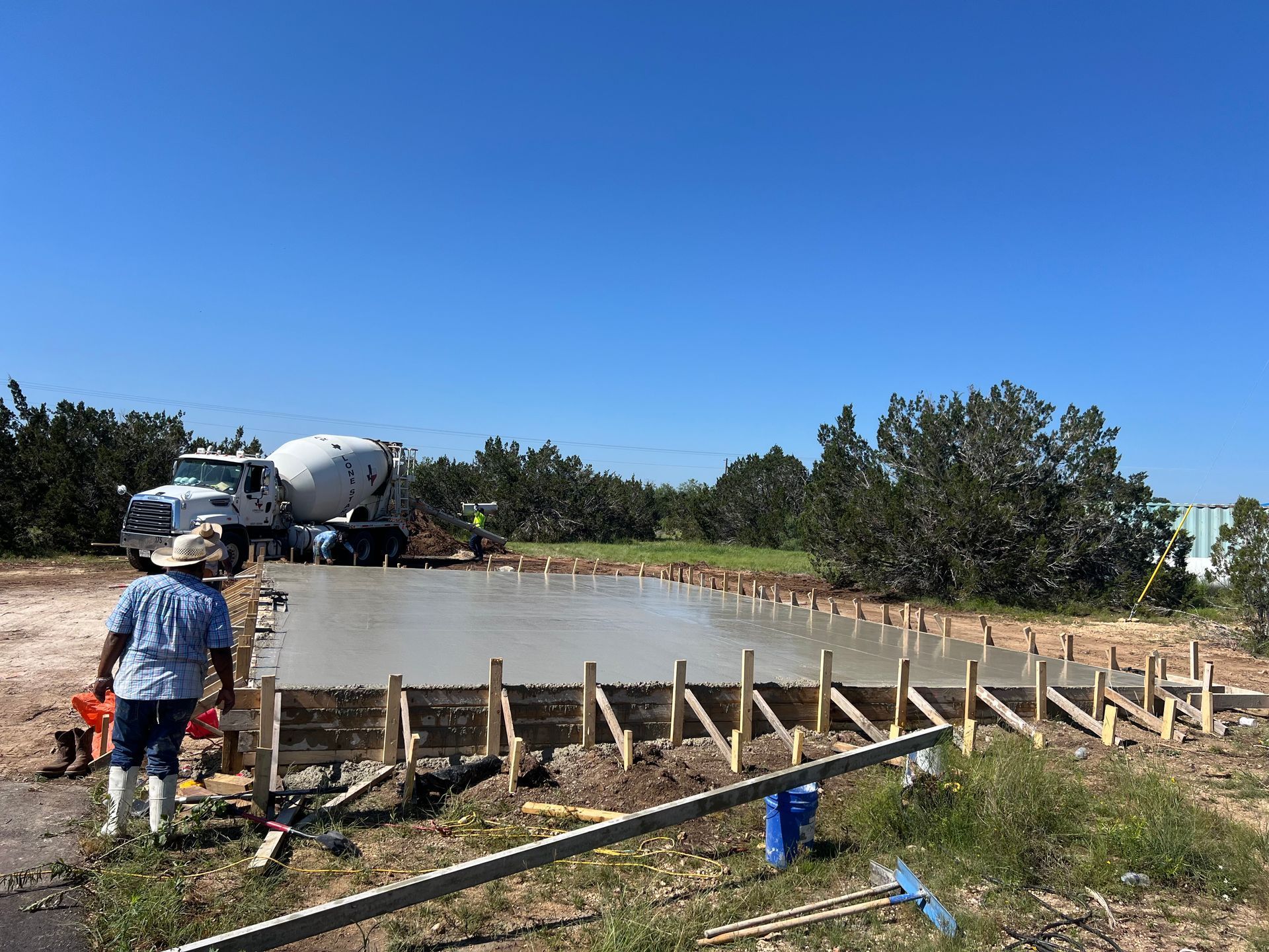 Concrete being poured into a wooden frame at a construction site; a cement truck and workers are present.