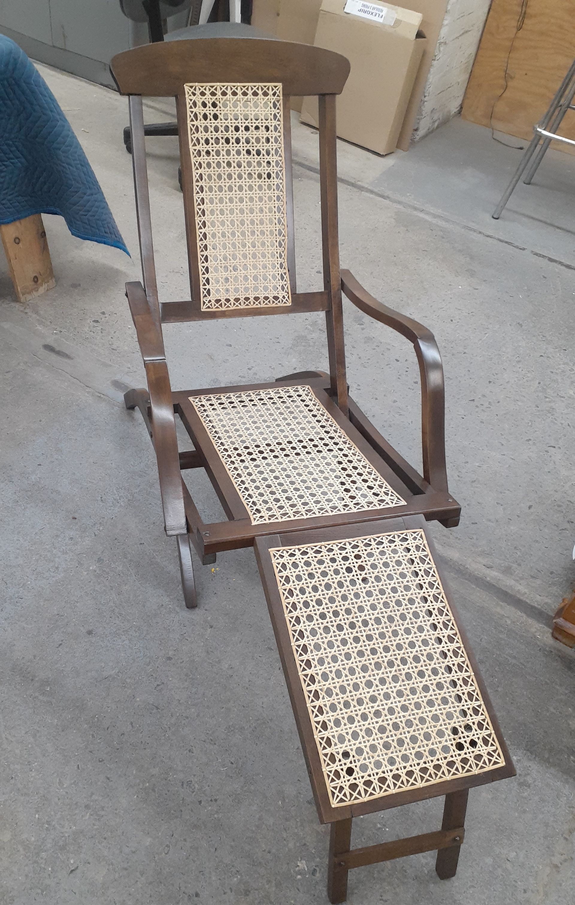 Wooden chair with woven cane seat and back, featuring a folding footrest or leg rest.