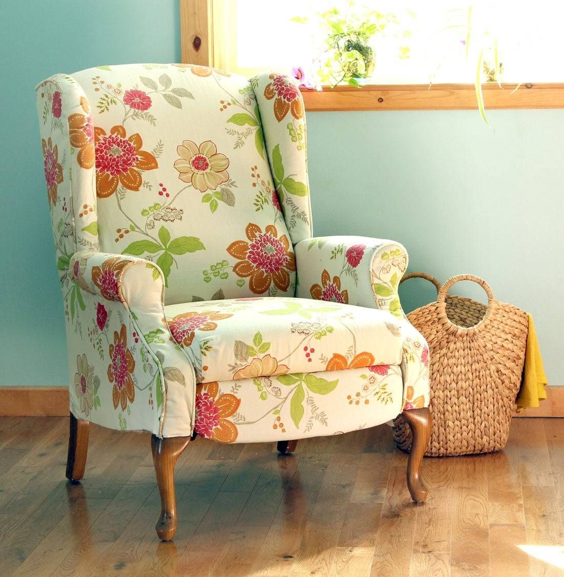 Floral upholstered armchair by a sunny window, with a woven basket beside it on a wooden floor