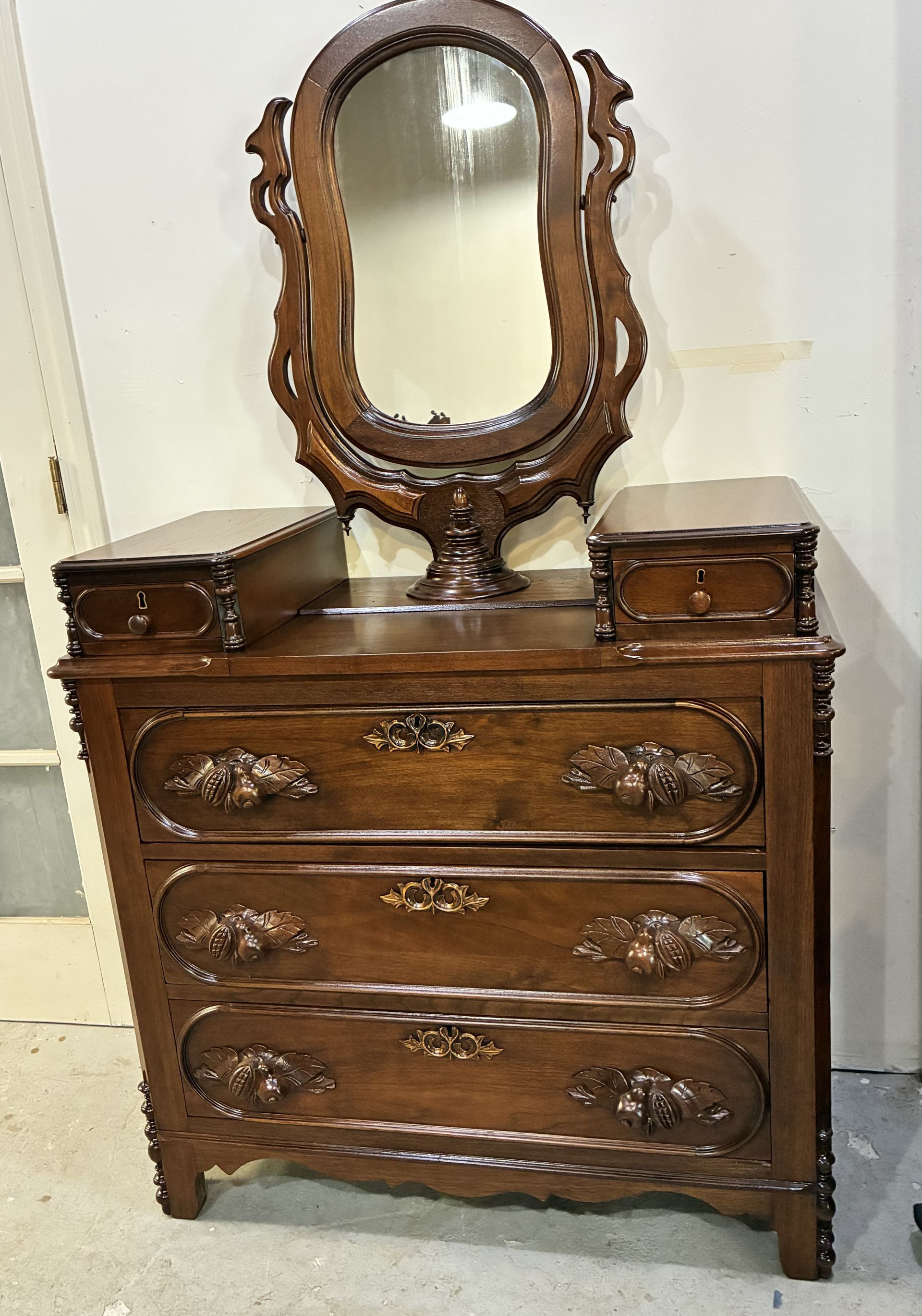 Ornate wooden dresser with oval mirror and matching side boxes against a wall