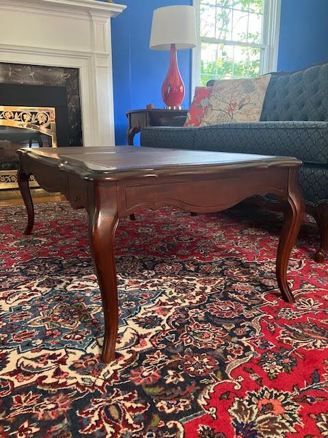 Dark wooden coffee table on a red patterned rug in a living room with a fireplace and blue sofa.