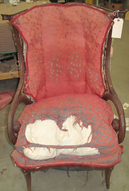 Worn red upholstered armchair with torn seat cushion and exposed white stuffing
